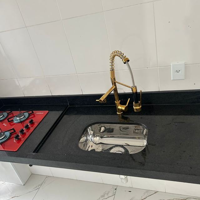 Bancada de granito preto com cooktop e torneira dourada